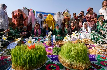 Tajiki Ismailis celebrating and posing for a picture in local dresses during their cultural festival in a group with food items in the front 