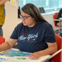 A candid photo of a girl dressed in blue shirt sitting and painting a picture