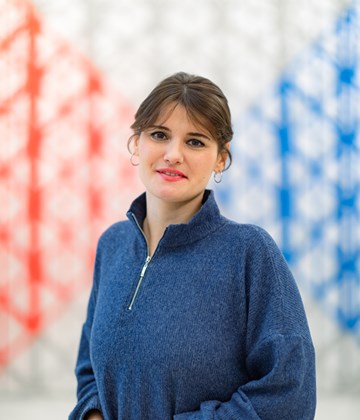 Woman in blue sweater standing in front of a wall with blue, read and white colours
