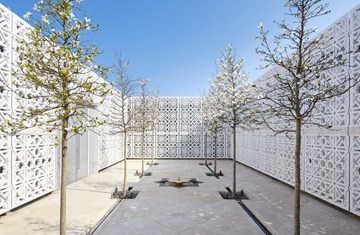 An image of AKC terrace with six trees on the side and a fountain in the centre surrounded with white geometrical designed walls