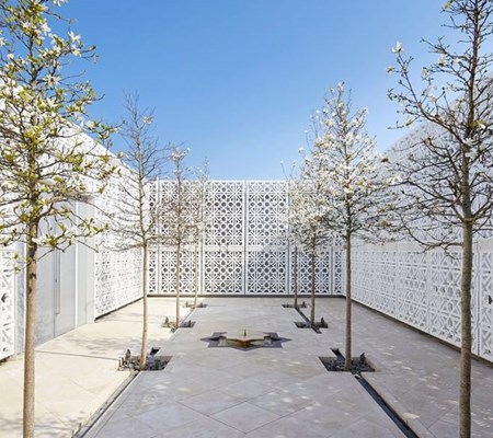 An image of AKC terrace with six trees on the side and a fountain in the centre surrounded with white geometrical designed walls