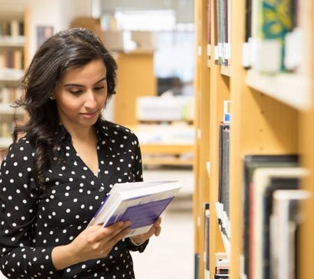 A STEP student in polka dot black dress standing in the corner of old IIS library (ground floor) and going through a book