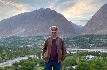 A man in brown leather jacket and beret standing in a hilly area of Chitral Pakistan smiling and posing