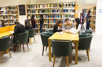 An overarching view from inside the IIS library with two students searching for books, three standing and reading, three sitting and studying their work while three others using one book to understand the content