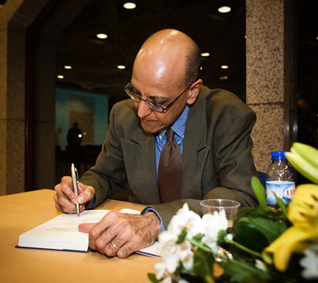 A man in grey suit sitting and signing a book