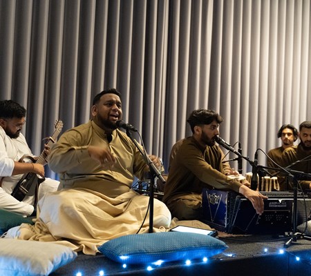 The Raag Qawwal Group performing, cross legged on cushions 