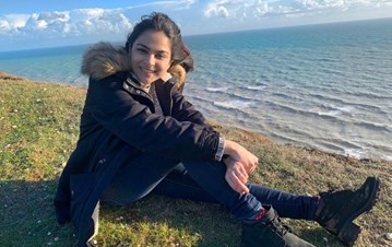 STEP student sitting in a garden wearing a winter jacket with her legs stretched in a sea view