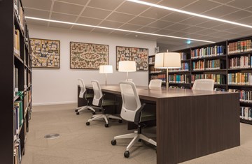 An image of the Aga Khan Centre library from inside with tables, chairs with lamps and book shelves on both sides and paintings on the wall