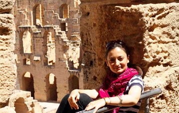 IIS employee Qudsia Shah sitting in an ancient architectural site holding a wall and posing for a picture
