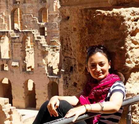 IIS employee Qudsia Shah sitting in an ancient architectural site holding a wall and posing for a picture