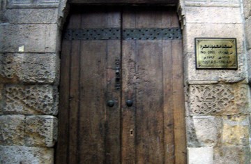 An image of an ancient door with Arabic written on the wall over it.
