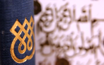 A side of a blue book cover with IIS logo on it and some blurry Arabic background 
