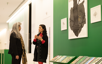 Professor Zayn Kassam listening to a lady explaining the image from the climate change exhibition in AKC gallery