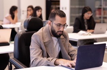 Male student in library sitting looking at laptop