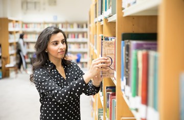 A student picking out a book from the library stack