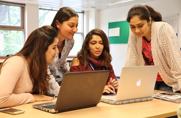 Two students sitting with their laptops, one student leaning on the table and a STEP faculty looking in the laptop and guiding them 