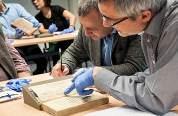 Two scholars working on a manuscript with gloves