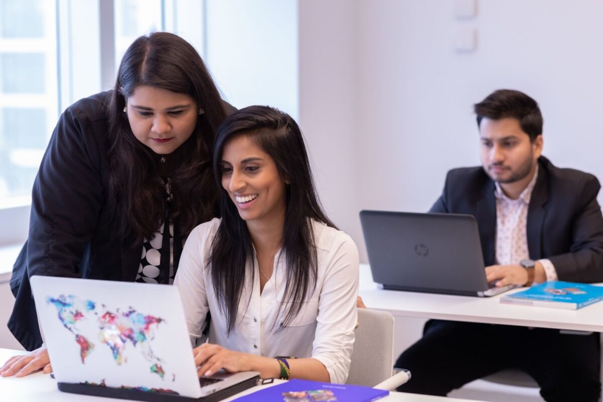 Two STEP students working together in a laptop, (one sitting while the other standing on her left) and the third STEP student working independently