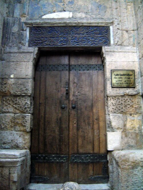 An image of an ancient door with Arabic written on the wall over it.