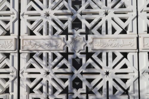 An image of geometric patterns carved in a grill with Arabic inscriptions written between them