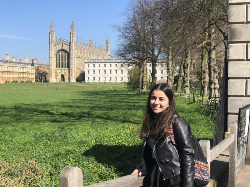 A STEP student named Mizhgona Okhonniyozo in black leather jacket and a backpack standing near a European building and posing for a picture