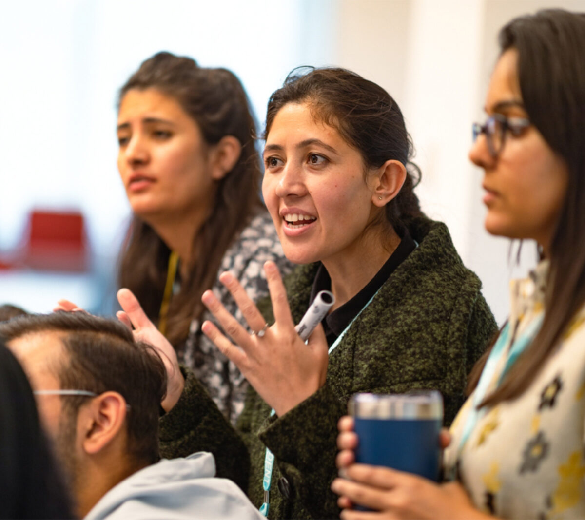 A side view of a student showing doing hand gestures and explaining something to the audience with one student each on left and right