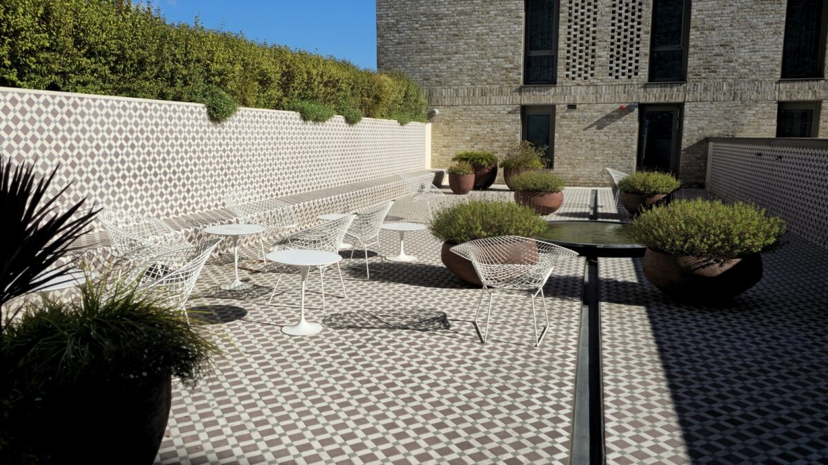 White wire chairs and round tables beside a tiled bench and potted shrubs on the garden terrace at Victoria Hall.