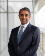 Alykhan Kassam, IIS Governor, smiling in rimless glasses, a navy suit and a light-blue tie.