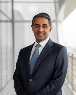Alykhan Kassam, IIS Governor, smiling in rimless glasses, a navy suit and a light-blue tie.