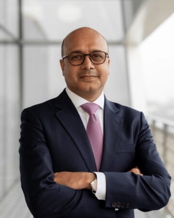 Arif Jamal, IIS Governor, smiling with arms crossed, wearing glasses, a navy suit and a patterned pink tie.