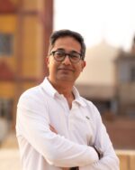 Fayaz Alibhai smiling with crossed arms outdoors.