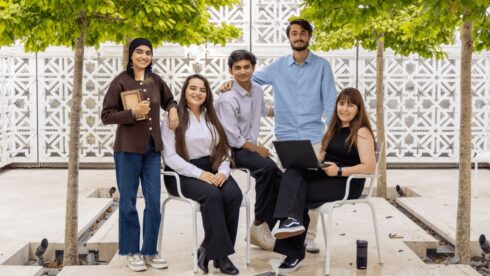 Five GPISH students gathered beneath trees in a courtyard with white geometric latticework screens.