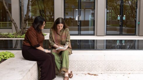 Two GPISH students sit beside a reflecting pool at Victoria Hall, looking at an open book together.