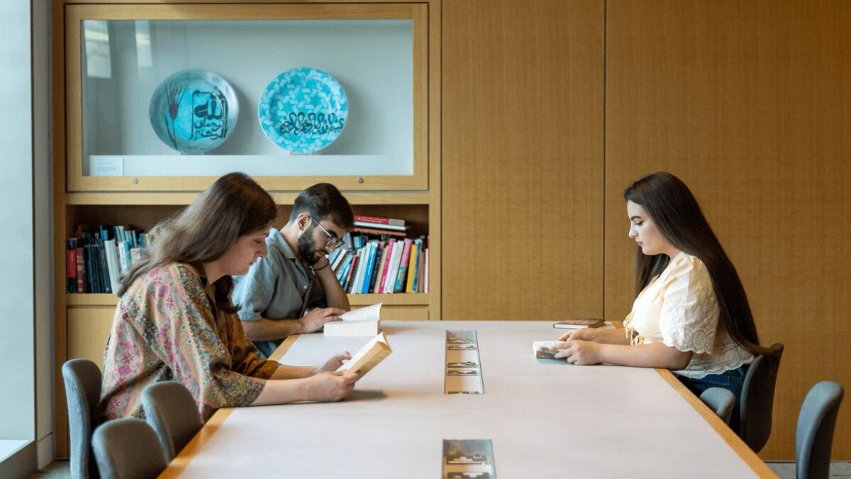 Three GPISH students read at a long table in the Victoria Hall reading room, beneath a display of calligraphic ceramic plates.