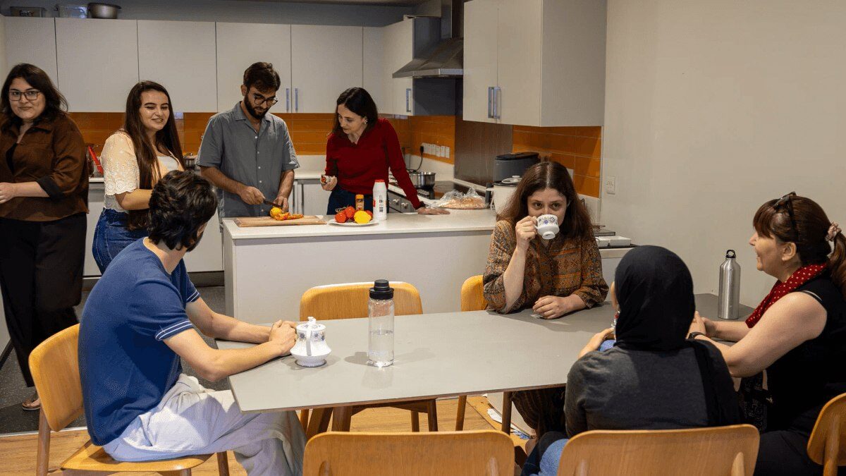 GPISH students prepare food at a kitchen counter and chat around a dining table in a shared kitchen at Victoria Hall.