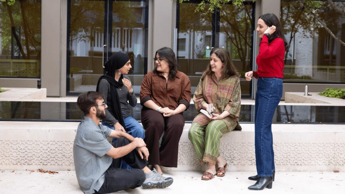 Five GPISH students talk and laugh together beside a reflecting pool on a terrace at Victoria Hall.