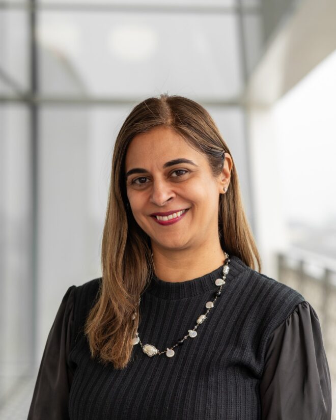 Karina Govindji, IIS Governor, smiling in a black knit top and a pearl and black-bead necklace.