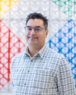 Dr Roy Wilson in checked shirt, posing against colourful background.