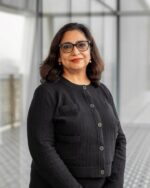 Tashmin Khamis, IIS Governor, smiling in black-framed glasses and a black textured jacket.