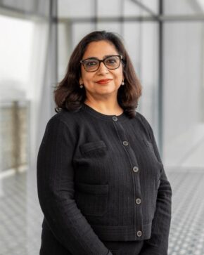 Tashmin Khamis, IIS Governor, smiling in black-framed glasses and a black textured jacket.
