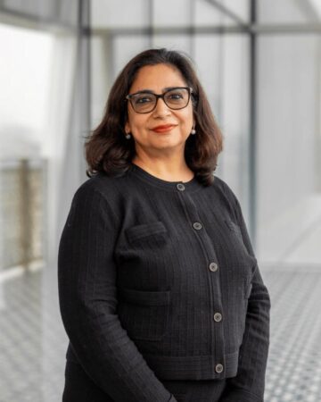 Tashmin Khamis, IIS Governor, smiling in black-framed glasses and a black textured jacket.
