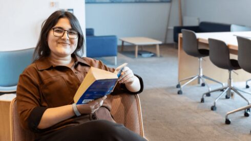 GPISH student Urooj smiles while reading a paperback in an armchair in a communal room at Victoria Hall.
