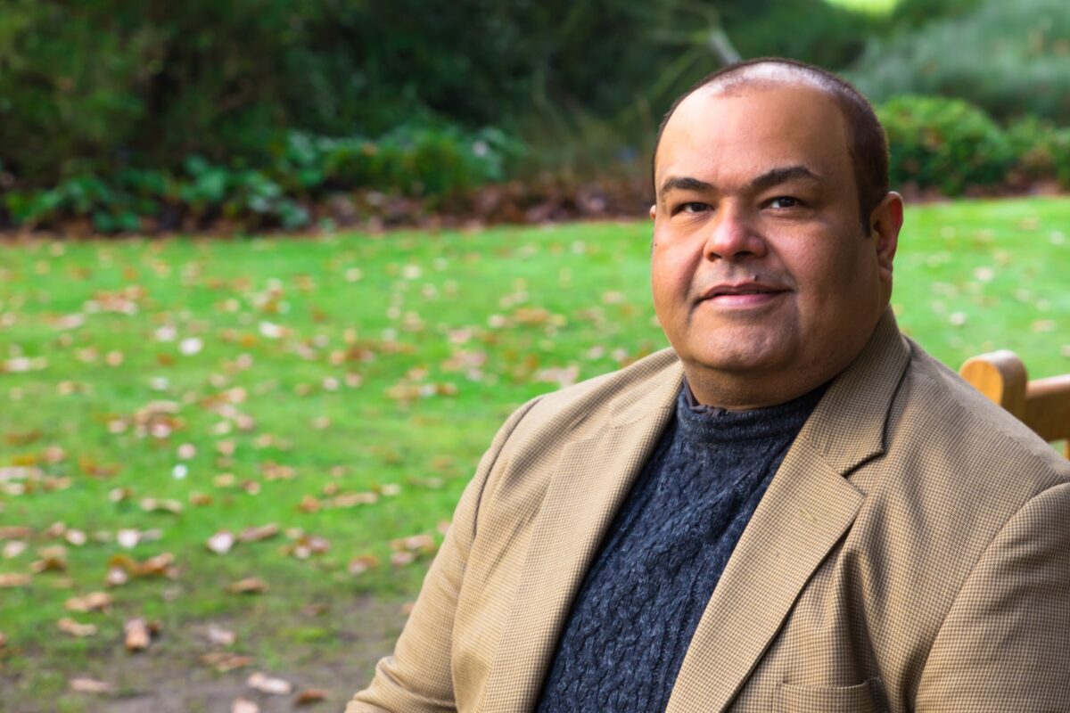 A man in light brown suit in a green outdoor background