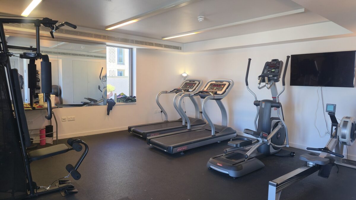 Fitness room at Victoria Hall with a multi-gym, dumbbell racks and cardio machines beside a large window.