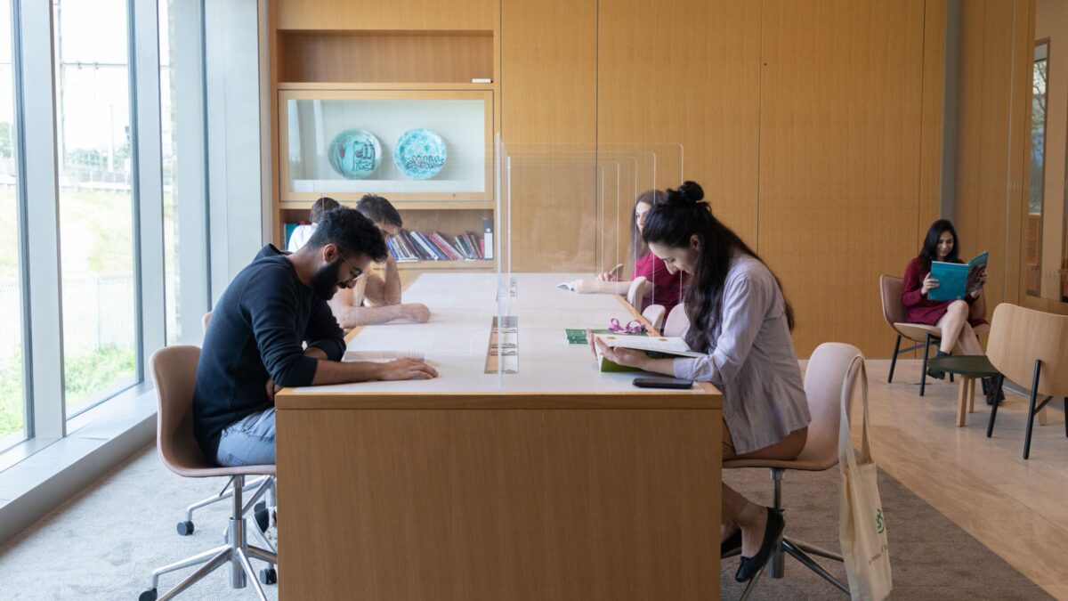 STEP students reading and studying at a long table in the Victoria Hall reading room, beside floor-to-ceiling windows.