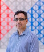 Man in checked shirt, front of colourful background.