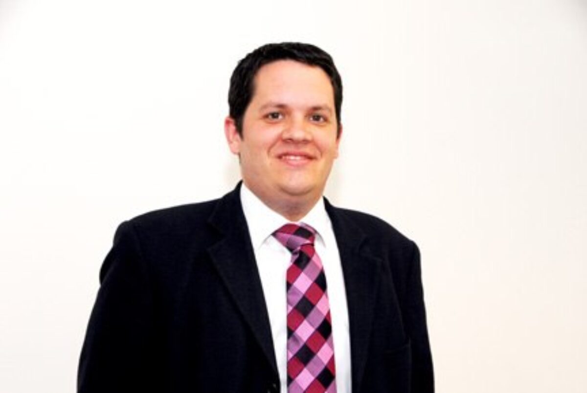 A man in black suit, white shirt, striped tie