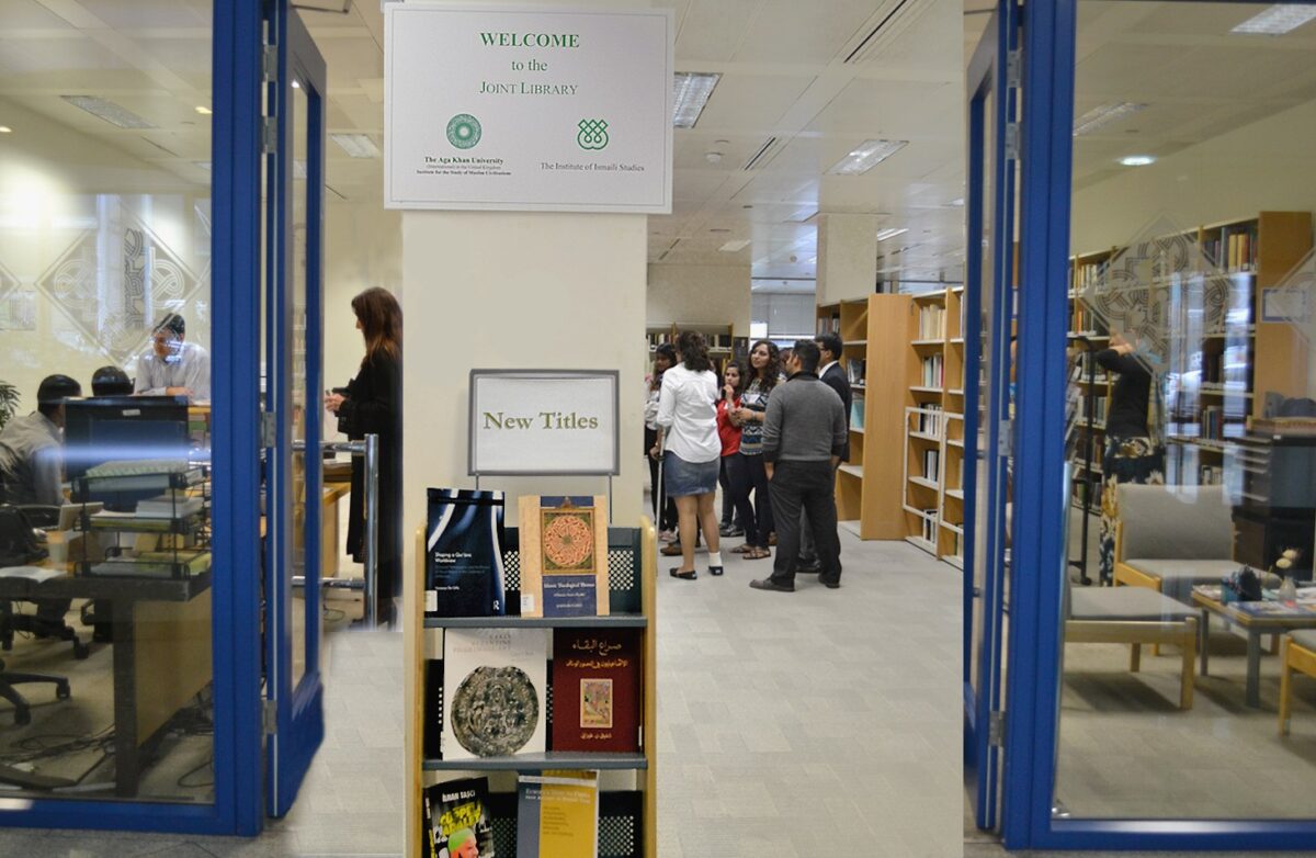 A photo from the library entrance with books in the front, books on the right hand side and group of people listening to someone