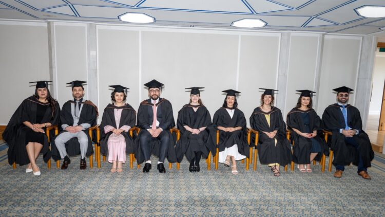 Nine GPISH graduates in black academic gowns and mortarboards seated in a row at their 2026 graduation.