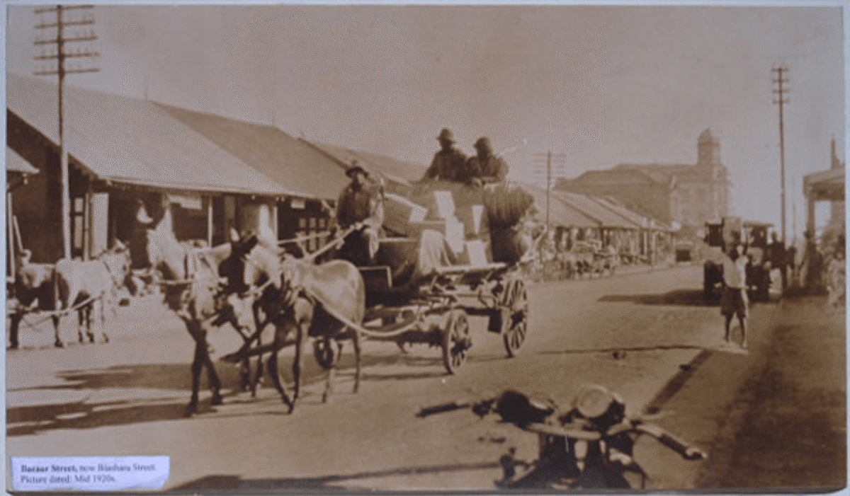Single-storey businesses, horse-drawn carriages, a motorcycle, and a jeep foreground Bazaar Street